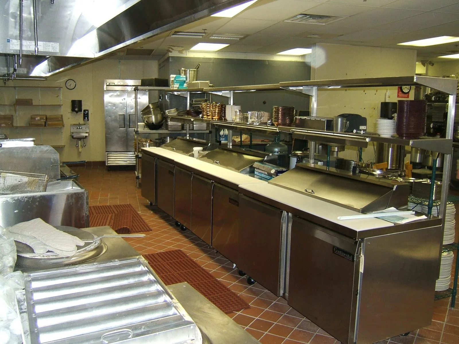 A commercial kitchen with stainless steel prep lines, refrigeration and an overhead exhaust hood