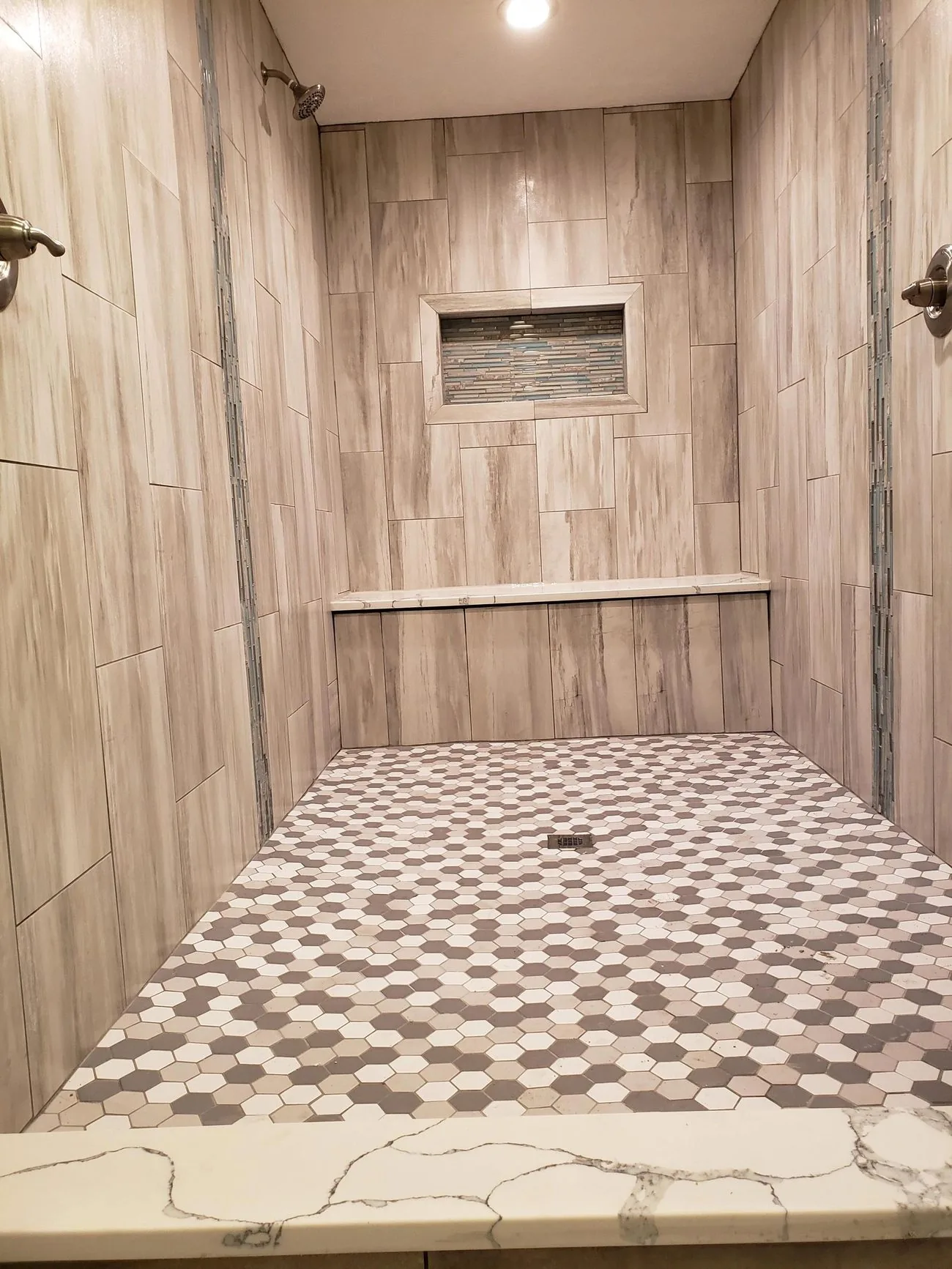 A walk-in shower finished in wood-look tile with a pebble floor and a built-in bench
