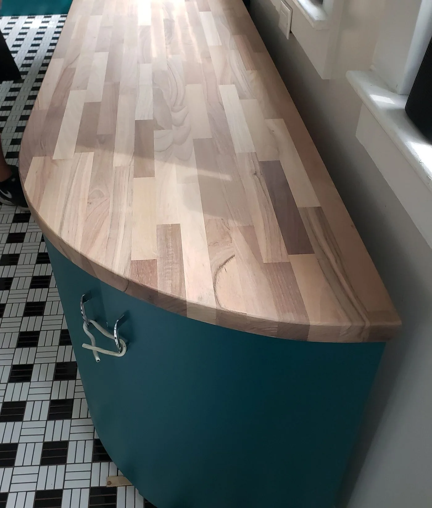 A butcher block bar top curving over a painted base above a mosaic tile floor