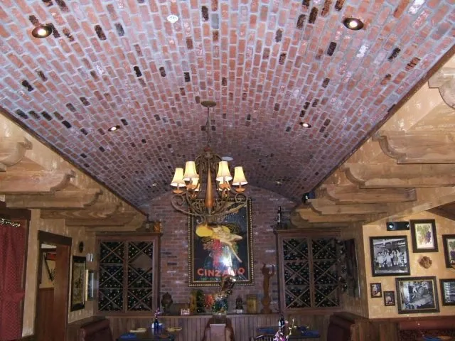 A brick barrel ceiling with a chandelier above a dining room