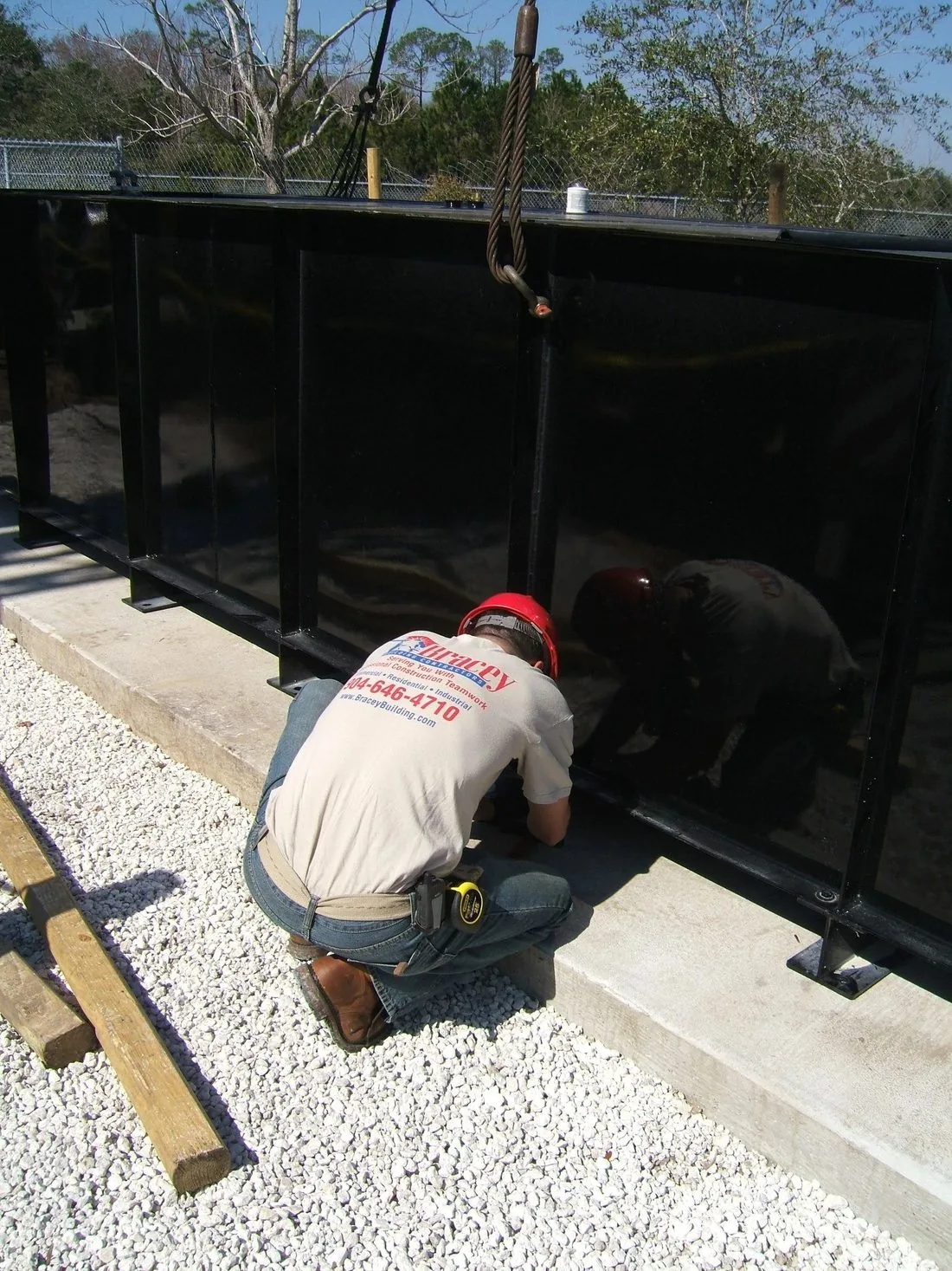 A worker setting a black fence panel on a fresh gravel bed