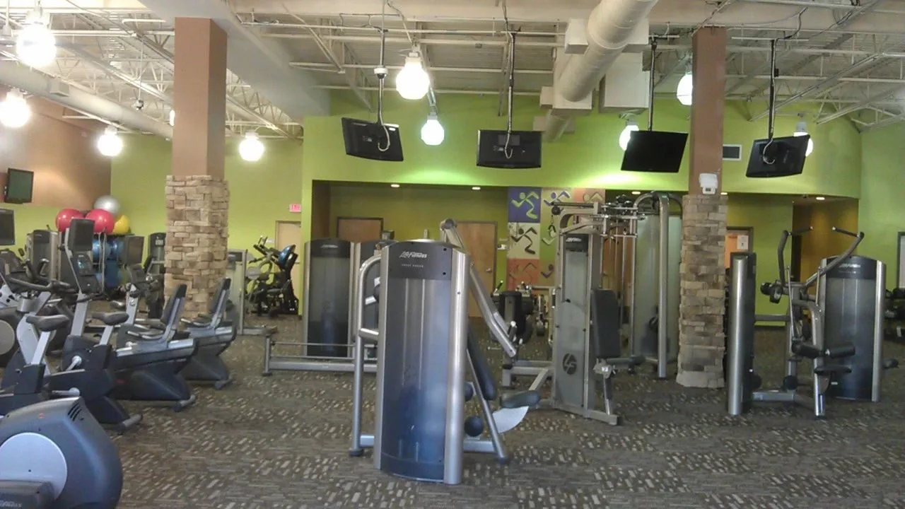 A fitness floor with equipment, exposed ceiling and brick columns
