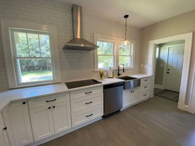 A white kitchen run with a farmhouse sink, quartz counters and a vented hood