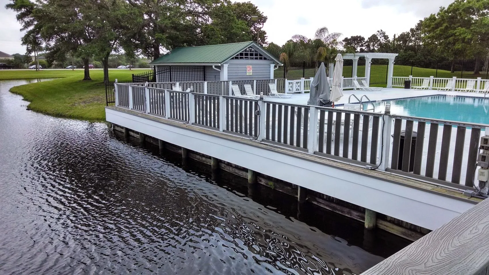 A white railing and deck running along the water beside a pool house