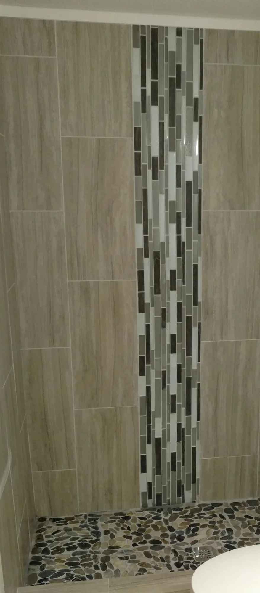 A tiled shower with a vertical glass mosaic inlay