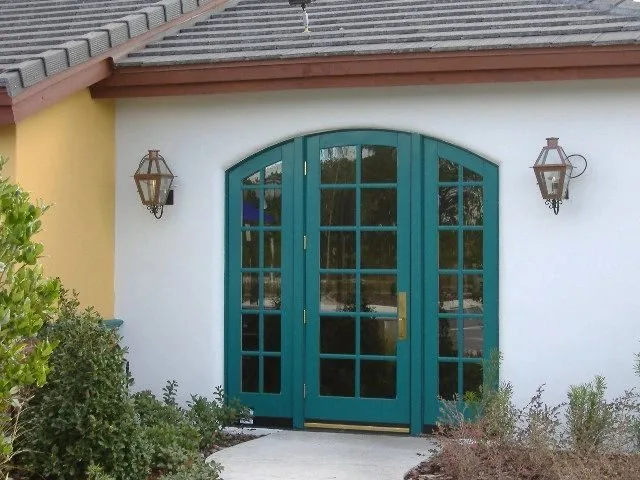 Arched teal entry doors with lanterns on a stucco building with a tile roof
